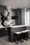 Corner of stylish Minimalistic grey kitchen, dark gray cupboards, white countertops and bar with stools. black sink and stove.