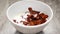 Cornflakes with chocolate flavor are flying from above into a white dish full of milk in slowmo