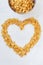 Cornflakes in a metal bowl on a painted white wooden background. The symbol of the heart is laid out of cornflakes.