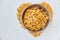 Cornflakes in a metal bowl on a painted white wooden background. The symbol of the heart is laid out of cornflakes.