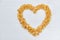 Cornflakes on a painted white wooden background. The symbol of the heart is laid out of cornflakes.