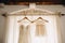 Cornice with white curtain and wooden hangers with bridesmaid dress and white baby dress.