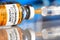 Coronavirus covid-19 vaccine concept -  glass bottle with silver cap on glossy white desk, orange syringe injected,  blurred blue