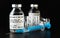 Coronavirus Covid-19 vaccine concept -  three glass vials on black table, blue hypodermic syringe needle near, closeup detail