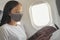 Coronavirus covid travel during pandemic Asian woman wearing face mask in cabin inside plane during flight reading