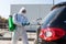 Coronavirus Pandemic. Disinfector in a protective suit and mask sprays disinfectants of car outdoors