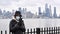 Coronavirus pandemic. Woman is wearing protection mask using smart phone on New York background