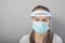 Coronavirus protection, health care and hygiene. Young woman in a protective mask screen with a visor on a gray background