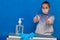 Coronavirus Samokarantin. A bottle of disinfectant gel and rubber gloves in the foreground and a guy in a face mask shows a liking