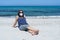 Coronavirus seaside holidays: a woman sitting on the sand at the beach look at the sun with the mask for Covid-19 pandemic