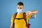 Coronavirus and travel bans. Displeased millennial guy with backpack wearing medical mask and showing thumb down gesture