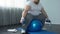 Corpulent male in sportswear lifting dumbbells sitting on fitness ball, activity