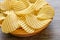 Corrugated golden potato chips in a wooden bowl.