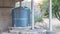 Corrugated steel water storage tank on top of flagstone masonry structure, with small stone fountain in front