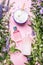 Cosmetic bottles and jars containers with green herbs and flowers on pink background, top view. Blank label for branding, mock-up.