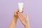 Cosmetic cream tube in womans hand on lilac background. Beauty concept. Packaging tube for cosmetic products