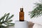 cosmetic face essential oil in amber glass bottle with dropper. oil standing on a grey cement podium next to pine branch