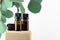 Cosmetic glass bottles with green eucalyptus leaves. Unbranded amber containers on wooden stand for essential, massage oil,