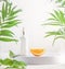 Cosmetic pipette bottle and orange slice on podium at white showcase background with green tropical leaves. Vitamin C serum.