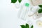 Cosmetic product bottle with micellar water or tonic for skin care, green leaves, white background with copy space, front view.