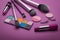 Cosmetic set of various shades compact and loose face powder, bronzed pearls, concealer and makeup brush on purple background.