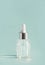 Cosmetic transparent liquid in glass bottle with dropper. Serum skin care product on light mint background, front view with copy s