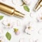 Cosmetics springtime Concept. Cosmetics, spring white flowers green leaves on light background. Cosmetic mock up gold bottles.