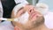 Cosmetologist is applying white moisturizing mask on man`s face using brush.