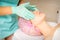 Cosmetologist with gloved hands applies a moisturizing mask with peeling cream on the female face. Facial cosmetology