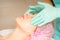 Cosmetologist with gloved hands applies a moisturizing mask with peeling cream on the female face. Facial cosmetology