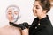 Cosmetologist in gloved hands with a smile applies a silver mask to a beautiful girl face with natural clean skin. Concept of