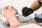 Cosmetologist hand in a protective rubber glove uses a special brush to apply a silver ointment to a female patient`s neck lyi