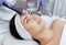 The cosmetologist makes the procedure an ultrasonic cleaning of the facial skin of a beautiful, young woman in a beauty salon.
