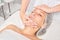 Cosmetologist massages cream mask into woman face skin for rejuvenation, procedure in beauty salon