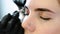 Cosmetologist performs the procedure of correction eyebrow with tweezers. Front eyes closeup view.