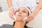 Cosmetologist removing facial cream mask from woman face skin with cosmetic wipes in beauty salon