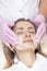 Cosmetology. Close up picture of lovely young woman with closed eyes receiving facial cleansing procedure in beauty salon.