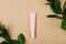 Cosmetology pink tube on minimalist beige background. Eye cream, foundation, concealer with green leaves on nude