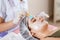 Cosmetology specialist applying facial mask using brush, making skin hydrated and healthy. Attractive woman relaxing