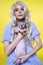 Cosplayer elf young woman holding Sphinx cat in her hands and showing it on yellow background