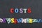 Costs word on black board background composed from colorful abc alphabet block wooden letters, copy space for ad text
