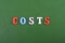 Costs word on green background composed from colorful abc alphabet block wooden letters, copy space for ad text