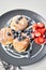 Cottage cheese pancakes or syrniki with blueberry and strawberries on black plate, closeup view. Condensed milk sauce