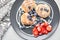 Cottage cheese pancakes or syrniki with blueberry and strawberries on black plate, closeup view. Condensed milk sauce