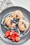 Cottage cheese pancakes or syrniki with blueberry and strawberries on black plate, closeup view. Condensed milk sauce