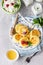 Cottage cheese pancakes, syrniki with honey, raspberry and mint on ceramic plate and homemade cottage cheese in a bowl.