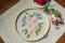 Cotton fabric with embroidered bouquet of wildflowers covered with wooden hoops, colored threads, scissors and a red pillow for ne