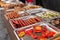 A counter with metal trays containing grilled sausages and meat. Food and cooking equipment at a street food festival