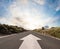 Country asphalt road in strong flare, road with arrow and blue sky with white cloud