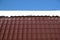 Country house roof from brown metal tile with snow in sunny spring day under blue sky